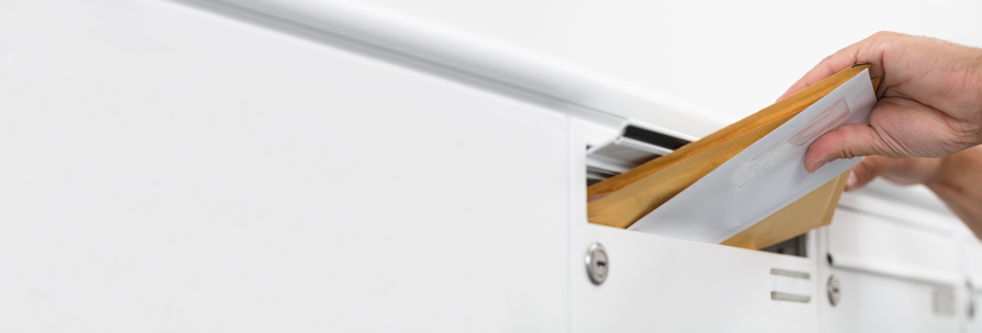 Brief wird in den Schlitz eines weißen Briefkastens geschoben.