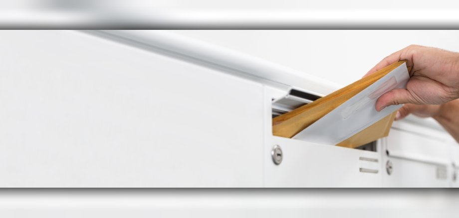 Brief wird in den Schlitz eines weißen Briefkastens geschoben.