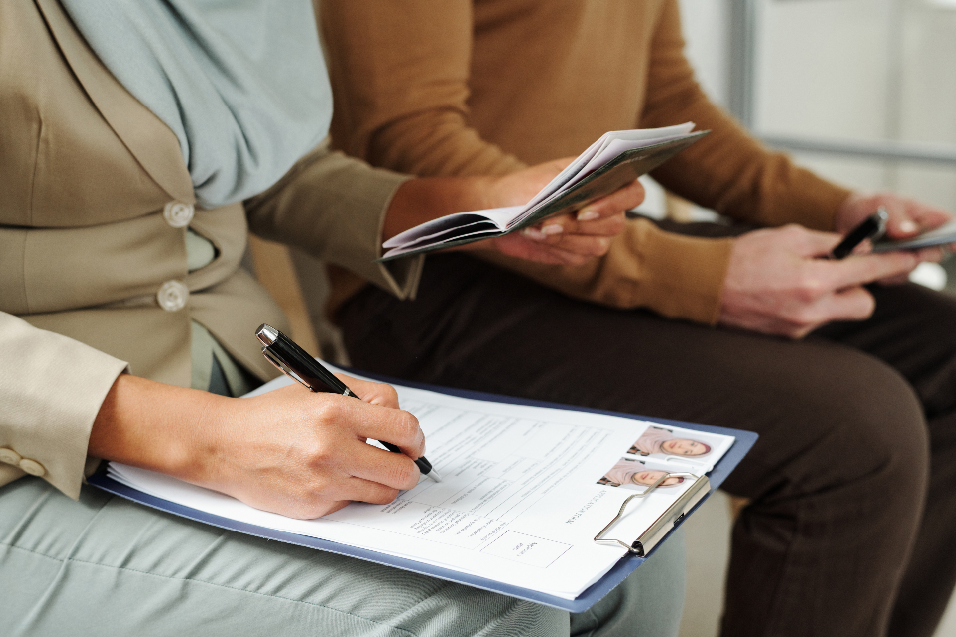 An unrecognisable woman sits on a chair in a government office and fills out an application form while waiting for her appointment.