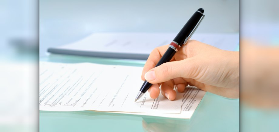 Hand mit schwarzem Stift unterschreibt ein Formular.