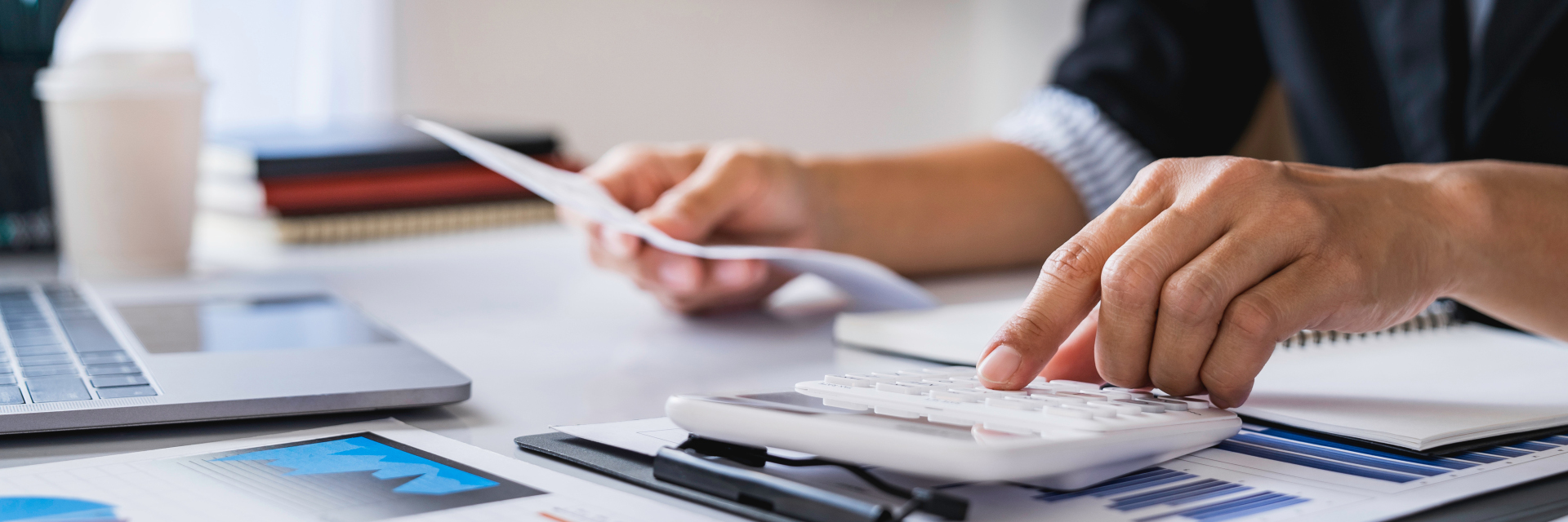 Mann am Laptop mit Taschenrechner und unterschiedlichen Dokumenten.