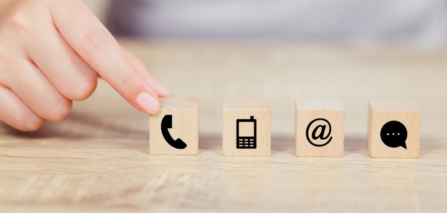 Hand und 4 Würfel mit Symbolen zum Thema Kontakt.