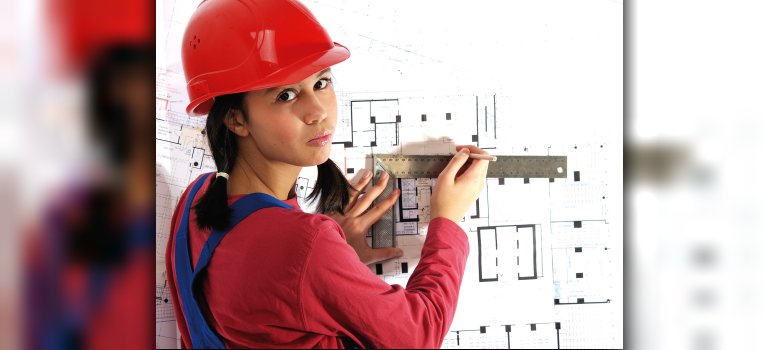 Frau mit rotem Helm am Reißbrett.