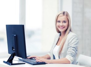 Frau bei der Büroarbeit vor Bildschirm und Tastatur sitzend.